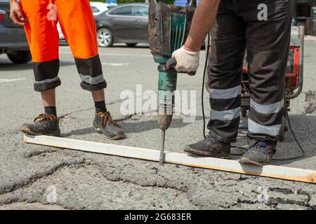 Il enlève l'asphalte avec un marteau à inertie. Retrait de la couche d'asphalte de la route. Le travailleur tient un marteau à inertie. Réparation sur route. Utilisation d'un hammam électrique Banque D'Images