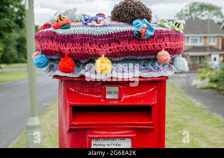 Basingstoke, Royaume-Uni - 3 juillet 2021 : décoration en crochet et laine tricotée sur une boîte de pilier rouge traditionnelle à Basingstoke, Hampshire. Le fil b Banque D'Images