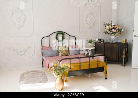 Intérieur de chambre néoclassique. Lit avec couvre-lit rose et oreillers gris. Fleurs dans un vase près du lit, commode brune, moquette et lit Banque D'Images