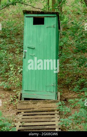 Ancienne toilette en bois vert dans un style rustique avec des escaliers et une fondation solide dans la forêt. toilettes en bois enfermées dans le parc. Structure verticale simple Banque D'Images