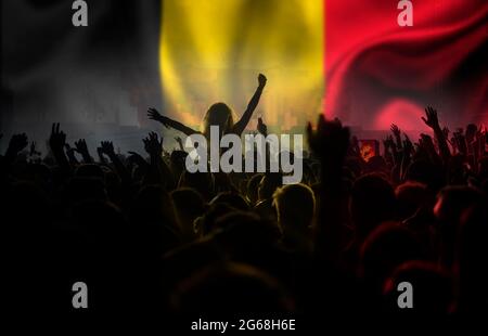 Fans de football soutenant la Belgique - la foule célèbre dans le stade avec les mains levées contre le drapeau de la Belgique Banque D'Images