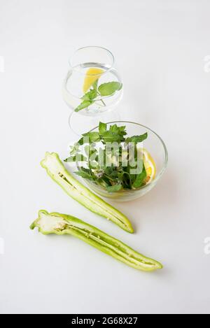 Bol en verre avec quartiers de citron et menthe fraîche. Verre à vin avec de l'eau de détox au citron infusée. Tranches de poivrons ​​green chauds. Désintoxication et chimie du corps Banque D'Images