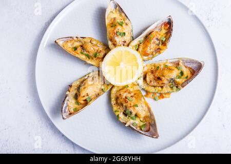 Moules de coquille de bœuf cuites dans une demi-coquille avec fromage, persil et citron sur une assiette blanche. Hors-d'œuvre chaud traditionnel. Gros plan, vue de dessus. Banque D'Images