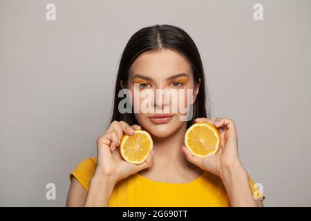 Parfaite jeune femme brunette avec une peau claire et une coiffure droite tenant des fruits de citron sur fond blanc. Alimentation, soin de la peau et soin du visage conc Banque D'Images