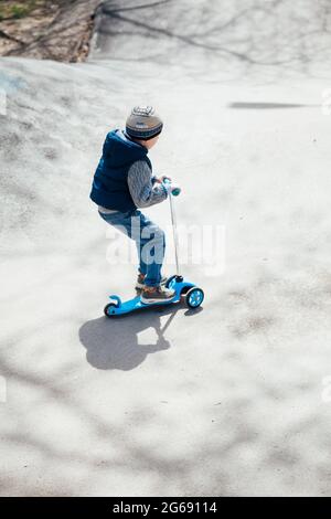 Un petit garçon fait un scooter sur les routes de la aire de jeux Banque D'Images