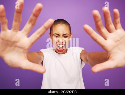 Portrait grand angle d'une femme hurlant avec les mains devant. Modèle femelle avec tête rasée sur fond violet. Banque D'Images