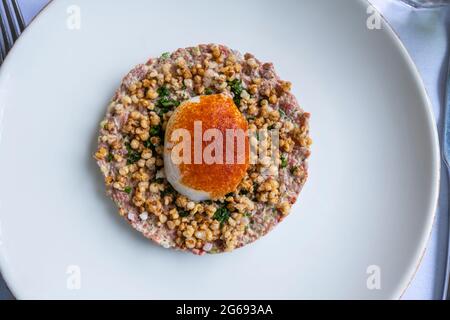 Steak tartare, plat de viande à base de bœuf haché cru (haché), assaisonné et servi avec un œuf légèrement poché sur une assiette blanche Banque D'Images