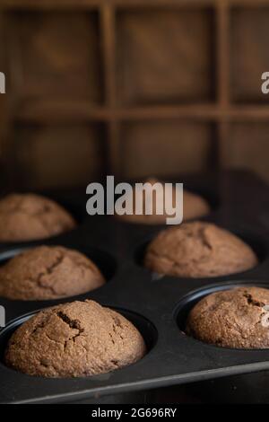 Petits gâteaux au chocolat maison fraîchement cuits dans un moule de cuisson, debout sur une table en bois. Banque D'Images