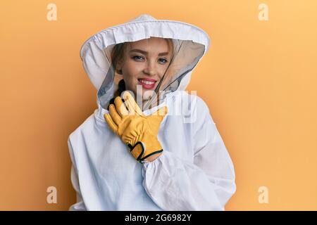 Belle blonde blanche femme portant un uniforme de gardien de beekeeper en regardant avec confiance la caméra souriant avec les bras croisés et la main levée sur le chi Banque D'Images