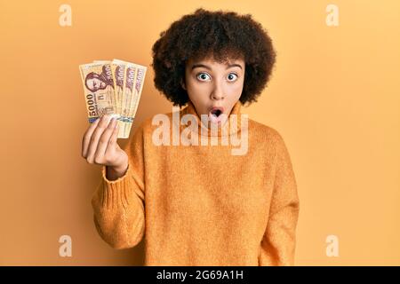 Jeune fille hispanique détenant 5000 billets de forint hongrois effrayé et stupéfié par la bouche ouverte pour la surprise, le visage incrédulé Banque D'Images