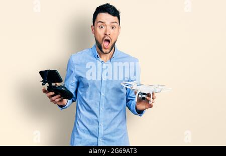 Homme hispanique avec barbe utilisant drone avec télécommande peur et choqué avec surprise et l'expression stupéfaite, la peur et le visage excité. Banque D'Images