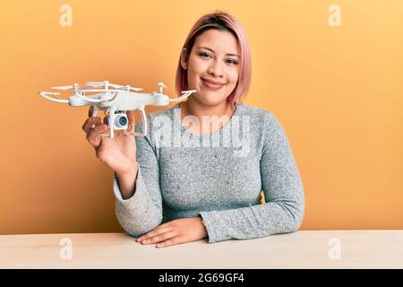 Femme hispanique aux cheveux roses utilisant un drone ayant l'air positif et heureux debout et souriant avec un sourire confiant montrant des dents Banque D'Images