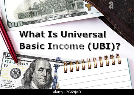 Photo TopView sur le thème du revenu de base universel. La question "Qu'est-ce que le revenu universel de base?", sur papier, entourée de billets en dollars, de bloc-notes, de mur Banque D'Images