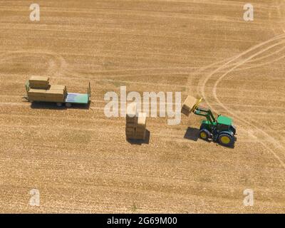 Vue de dessus d'un tracteur vert chargeant des balles de paille sur une remorque, photo prise avec un drone. Banque D'Images