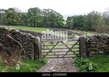 Ancienne porte de ferme en bois menant vers le bas d'une piste avec des murs en pierre sèche et des arbres Banque D'Images