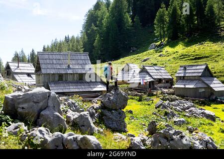 Femme debout sur un rocher et regardant les cabanes de berger à Planina Visevnik dans les collines au-dessus de Bohinj, Slovénie Banque D'Images