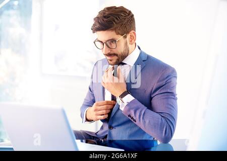 Shot of young businessman wearing suit alors qu'il était assis au bureau et nœud de cravate. Banque D'Images