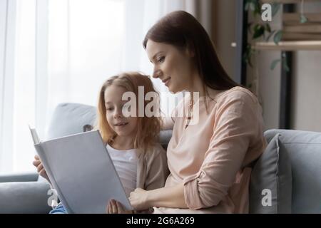 La mère et la fille d'âge scolaire intéressées lisant le livre sur le canapé Banque D'Images