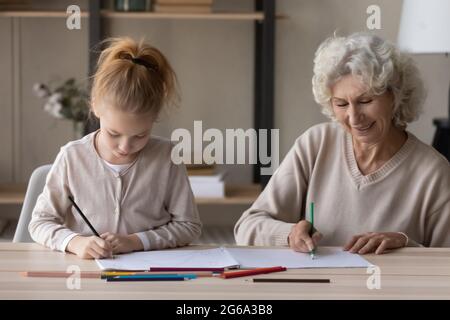 Grand-mère senior attentionnée aider grand-enfant de la préadolescence à peindre le livre de coloriage Banque D'Images