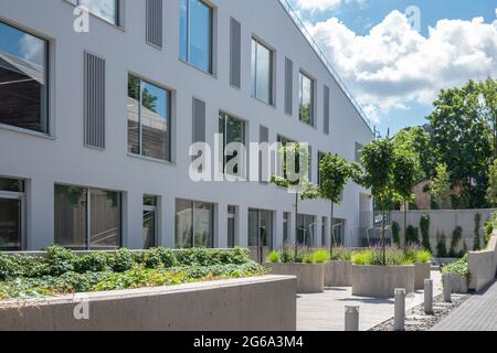 Nouvelle façade de bâtiment et aménagement urbain moderne avec bancs en béton, plantes vertes, pots de fleurs Banque D'Images