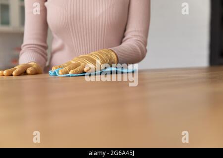 Gros plan une jeune femme nettoie la table en bois avec des gants. Banque D'Images