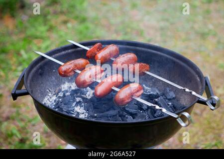 set de cuisson jour ensoleillé, saucisses de viande de barbecue sur la grille du gril. pince pour gril. Dans l'arrière-plan légèrement flou. Banque D'Images