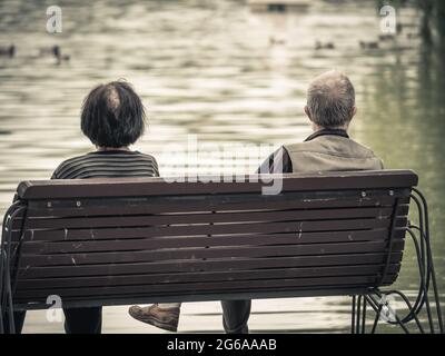 Image vintage avec deux aînés assis sur un banc dans un parc et regardant le lac Banque D'Images