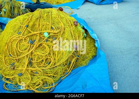 Filets de pêche séchant sous le soleil dans le port de pêcheur. Les filets de pêche de couleur jaune s'accumulent sur un fond bleu. Matériel de pêche Banque D'Images