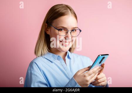 Portrait émotionnel de sourire heureux positif Manager employé de bureau en lunettes utiliser smartphone. Femme dans un shirtwrites bleu un message sur le téléphone isolé Banque D'Images