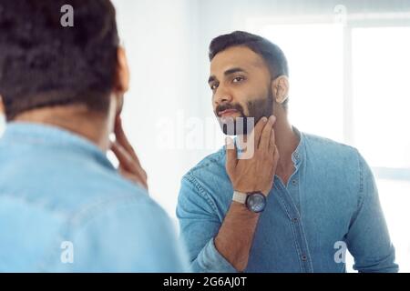 Curieux Indien attentionné touchant la barbe sur le visage regardant le miroir Banque D'Images