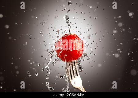 cerise de tomate sur une fourchette dans des éclaboussures d'eau. Arrière-plan noir et blanc Banque D'Images