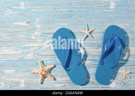 des tongs en caoutchouc bleu et des étoiles de mer sur un fond en bois bleu, vue d'en haut Banque D'Images