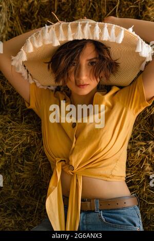 Portrait d'une femme avec un chapeau de paille, chemise jaune assise dans un grenier. Banque D'Images