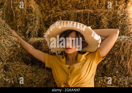 Portrait d'une femme avec un chapeau de paille, chemise jaune assise dans un grenier. Banque D'Images