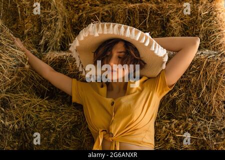 Portrait d'une femme avec un chapeau de paille, chemise jaune assise dans un grenier. Banque D'Images