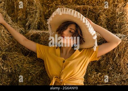 Portrait d'une femme avec un chapeau de paille, chemise jaune assise dans un grenier. Banque D'Images