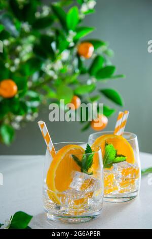 Deux cocktails de fruits rafraîchissants à l'orange, à la menthe et à la glace sur une table blanche avec un fond d'agrumes. Boissons du bar en été. Carte Vertucal. Fi sélectif Banque D'Images
