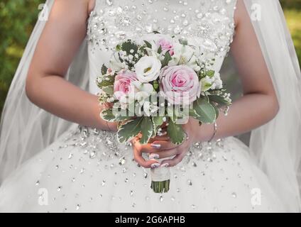 Les mains de la mariée dans une robe blanche de mariage tiennent un bouquet de fleurs gros plan. Banque D'Images