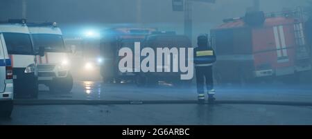 Panorama de rue fermée dans la fumée due à l'incendie avec de nombreuses ambulances auto, pompiers camions et sauveteurs voitures et paramédics. Le secouriste est au centre, vue de l'arrière. Accidents et catastrophes. Banque D'Images