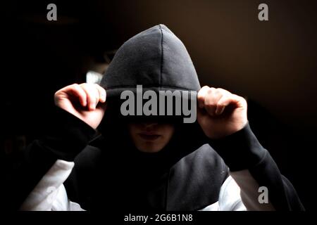 homme anonyme dans la cagoule sombre debout dans la pose mystérieuse Banque D'Images