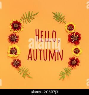 Texte et cadre Hello Autumn à partir de fleurs rouges jaunes sur fond orange. Vue de dessus plat carte de vœux invitation. Banque D'Images