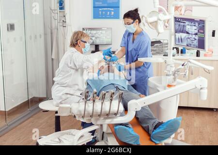 Dentiste médecin et infirmière médicale effectuant un nettoyage professionnel des dents chez un patient malade pendant un examen stomatologique au cabinet dentaire. L'équipe de l'hôpital examine les maux de dents qui préparent le traitement dentaire Banque D'Images