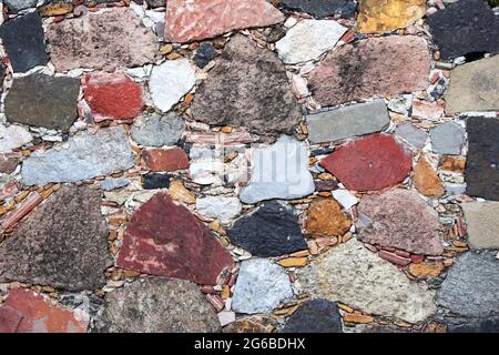 Texture du mur avec des blocs de pierre de couleurs rouge, jaune, vert et gris. Arrière-plan horizontal avec mosaïque décorative en pierre Banque D'Images