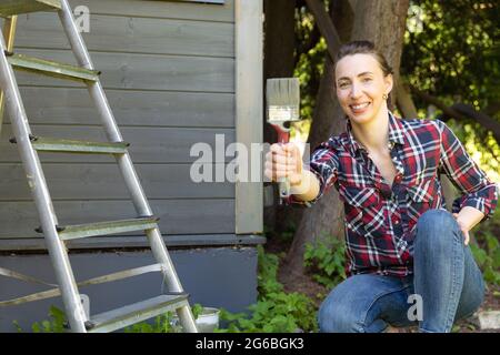 Femme en travail de focad peinture maison en bois mur extérieur avec pinceau et bois couleur de protection maison concept d'amélioration. Banque D'Images