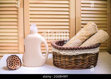 Gel pour laver le linge dans une bouteille en plastique près d'une pile de serviettes propres dans le panier. Composition sur étagère en bois blanc sur fond en bois. Banque D'Images