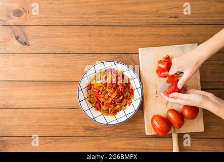 Détail des mains d'une femme qui pelent les tomates avec un couteau. Préparation de poivrons rôtis, un plat typique de cuisine espagnole et andalouse. Banque D'Images