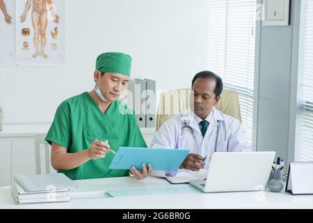 Médecin généraliste sérieux et son collègue discutant des examens médicaux du patient assis à la table de bureau Banque D'Images