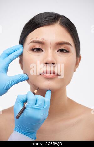 Le chirurgien en plastique dessine des lignes sur le visage de la jeune femme avant d'injecter de l'acide hyaluronique ou du botox Banque D'Images