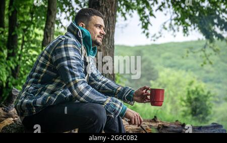 Un homme avec une tasse de boisson chaude se réchauffe par le feu dans la forêt. Banque D'Images