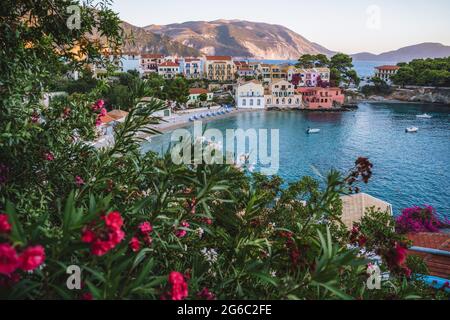 Village d'Assos à la lumière du soir sur Kefalonia, Grèce. Fleur rouge en face de la baie turquoise et des maisons traditionnelles colorées Banque D'Images